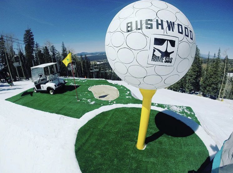 A giant Bushwood golf ball on a tee atop artificial turf, with a flag, sand trap and golf cart set up as a terrain park feature